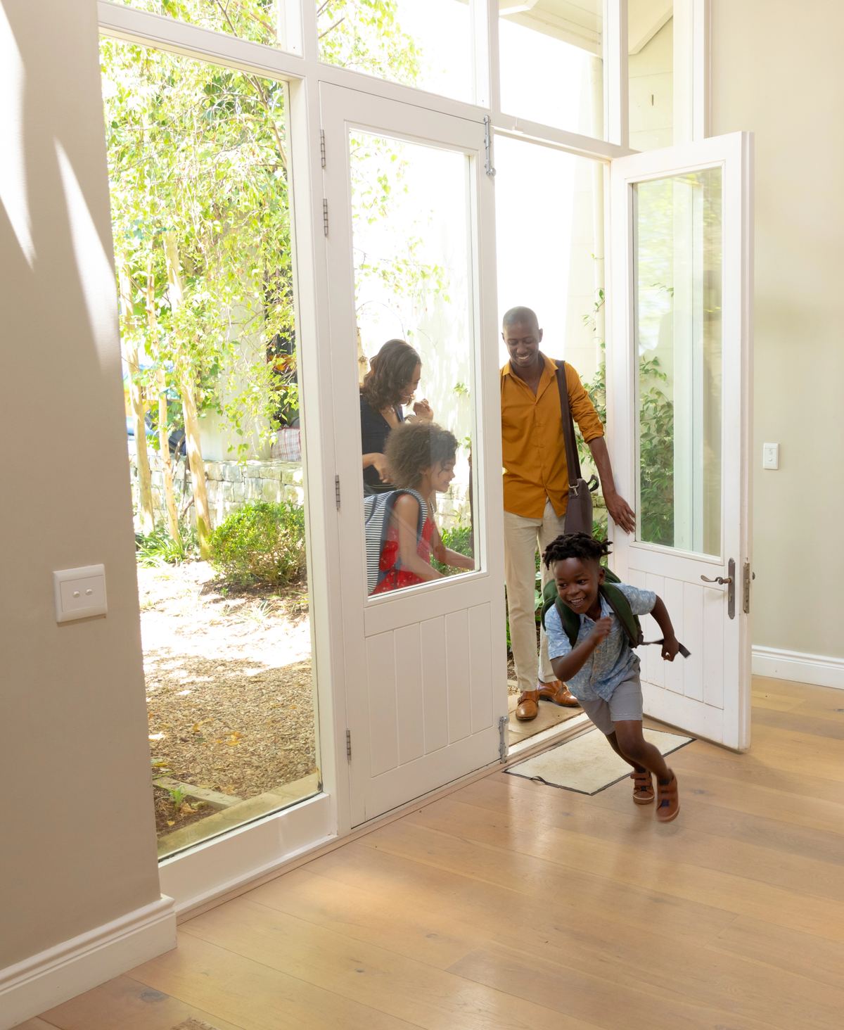 A family arriving through the open front door of a bright hallway